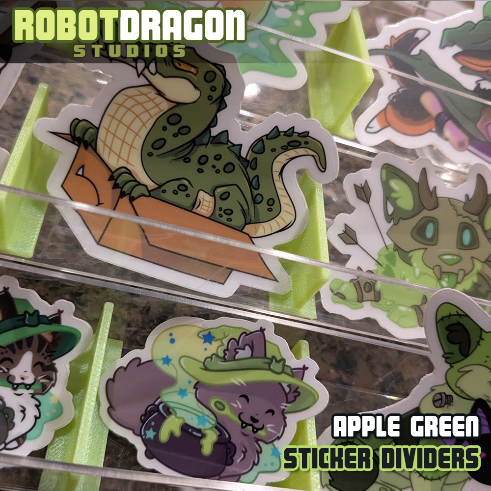 Example of 3D printed apple green iridescent PETG sticker dividers in use in a sticker display designed and created by Robot Dragon Studios for artist alley, also visible are Wizard Corgis, Croc in a Box, Witch Kitties, Gelatinous Necroloaf, and Buster Frankencorgi.