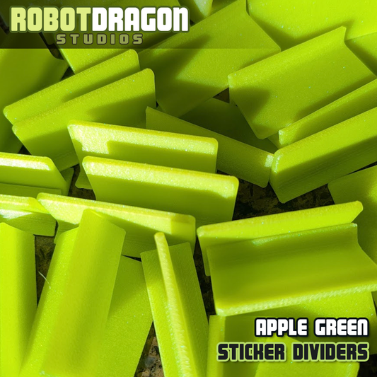 Close up photo of a messy pile of 3D printed apple green iridescent PETG sticker dividers designed and created by Robot Dragon Studios for artist alley.