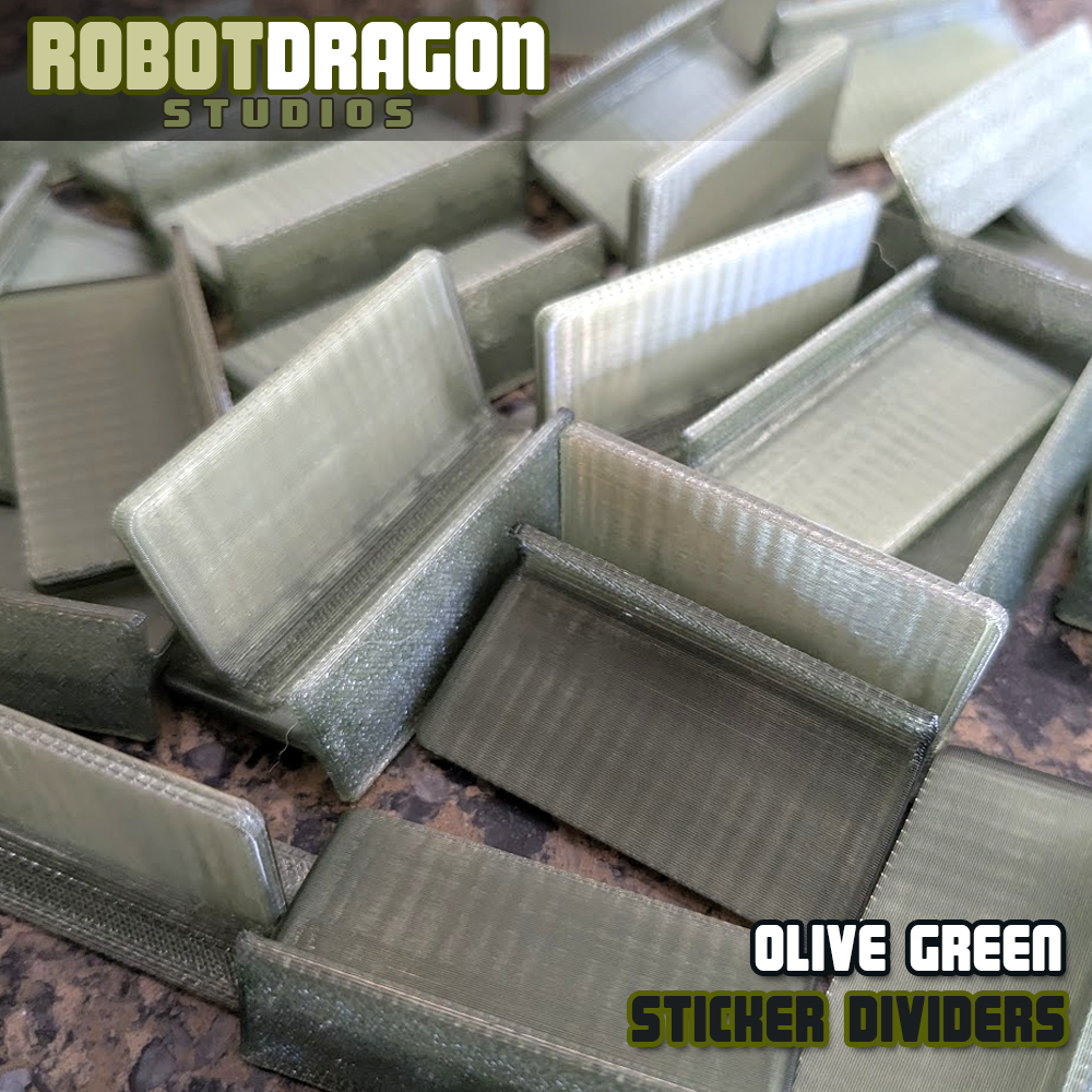 Close up photo of a messy pile of 3D printed olive green translucent PETG sticker dividers designed and created by Robot Dragon Studios for artist alley.